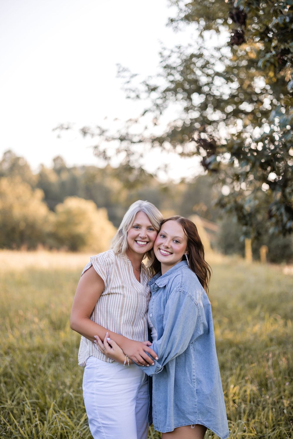 Two friends share a joyful embrace while posing together in a sunlit field at golden hour.