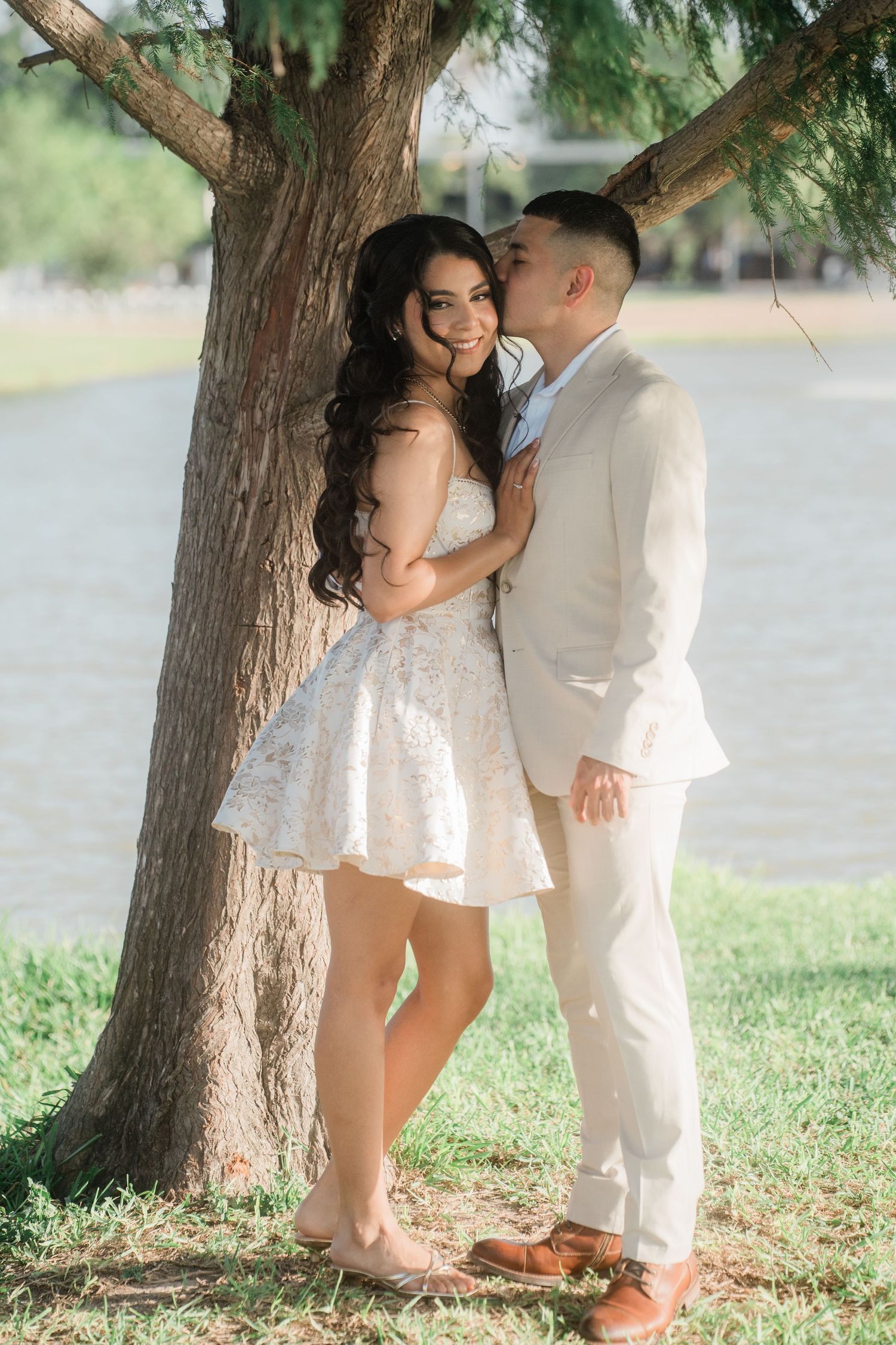 A couple shares an intimate moment under a large tree in a park setting.