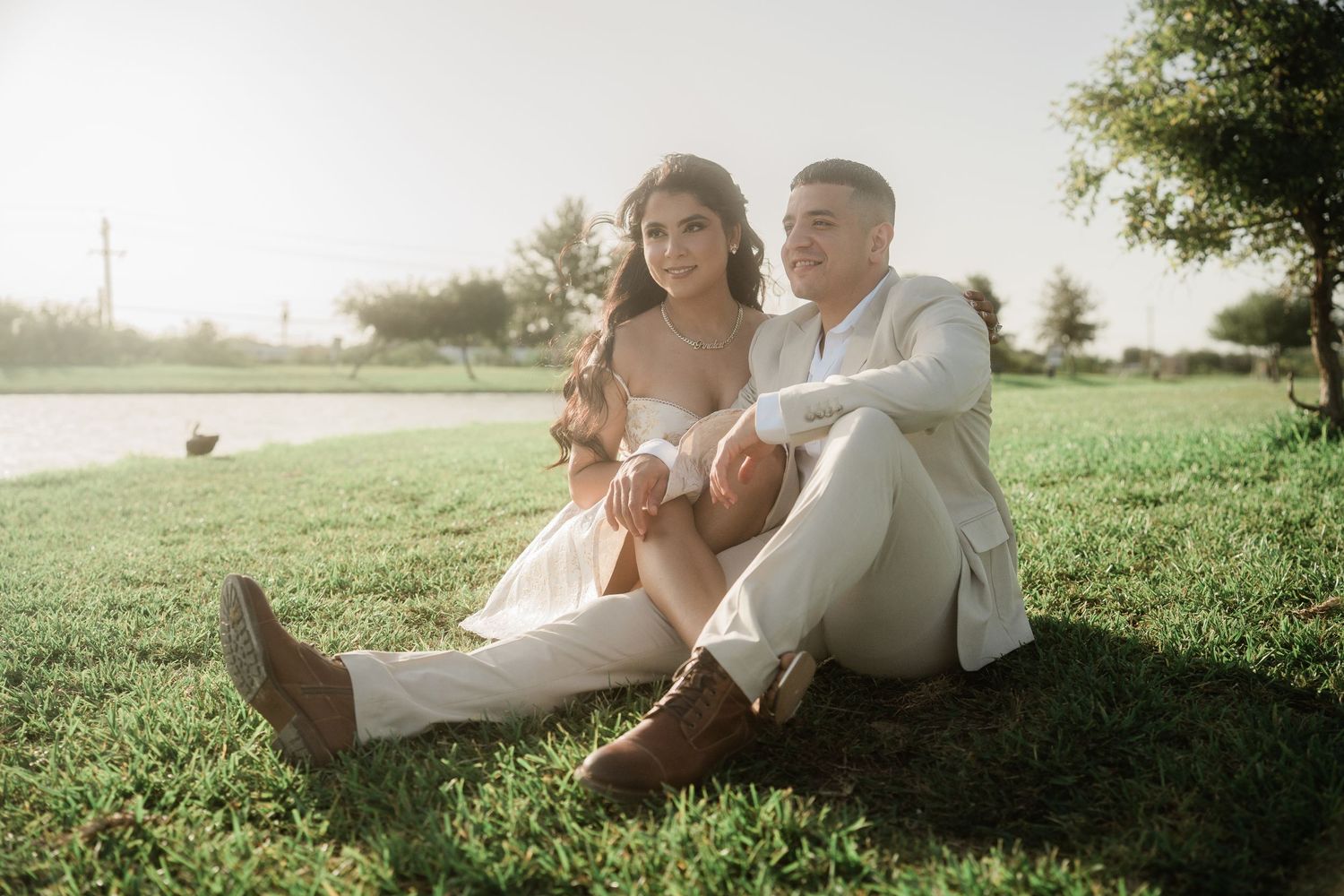 A couple relaxes on grass during golden hour for engagement photos.
