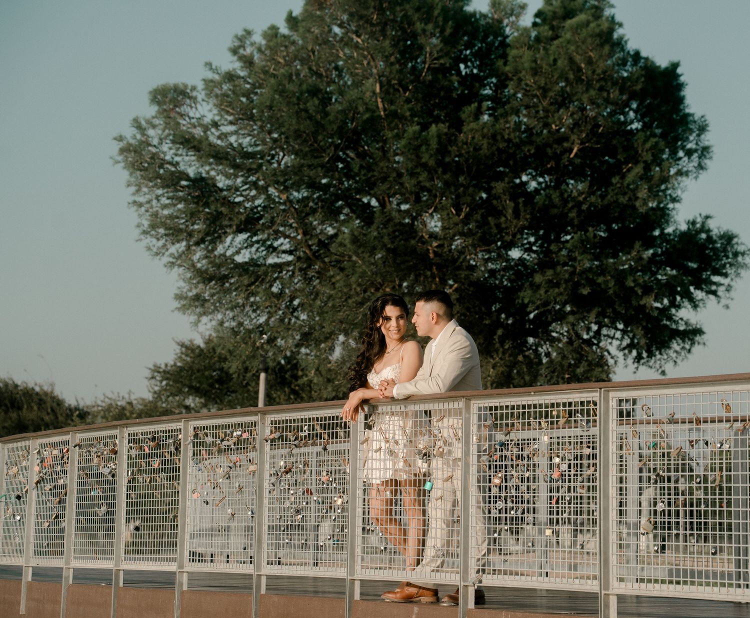 A couple sits together on a decorative bridge railing during sunset.