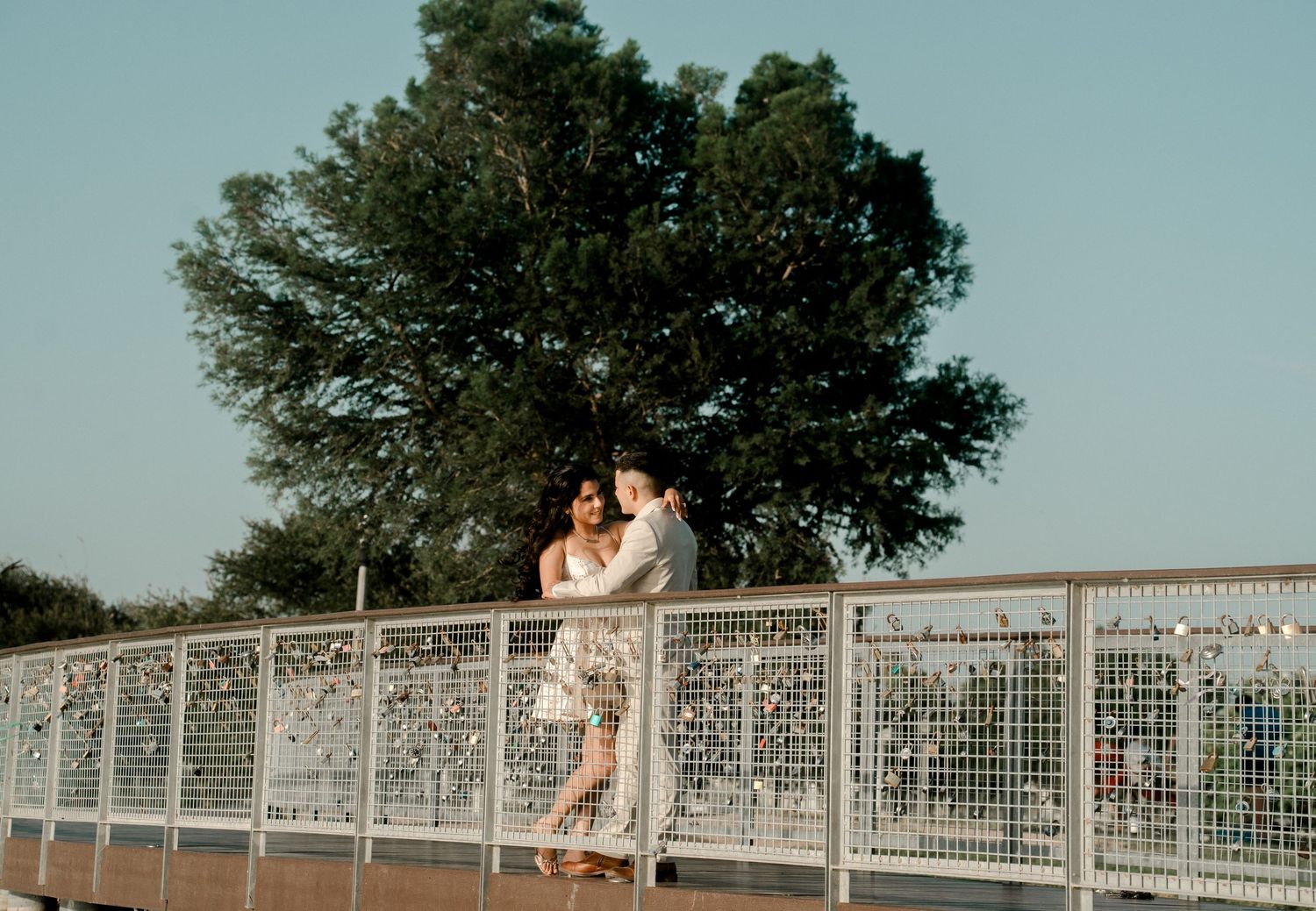 A couple enjoys a romantic moment on a bridge with ornate railings at dusk.