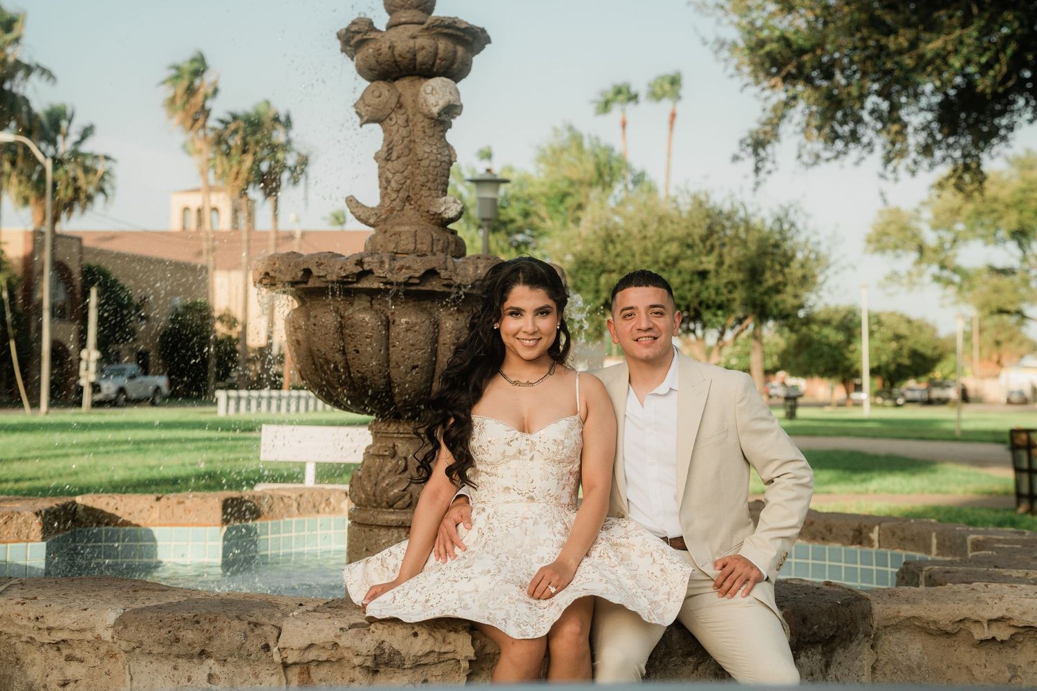 A couple shares a tender moment on a decorative stone bench surrounded by palm trees.