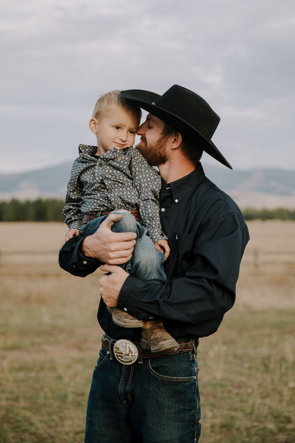 A tender moment between parent and child in a rustic field with mountains in the background.
