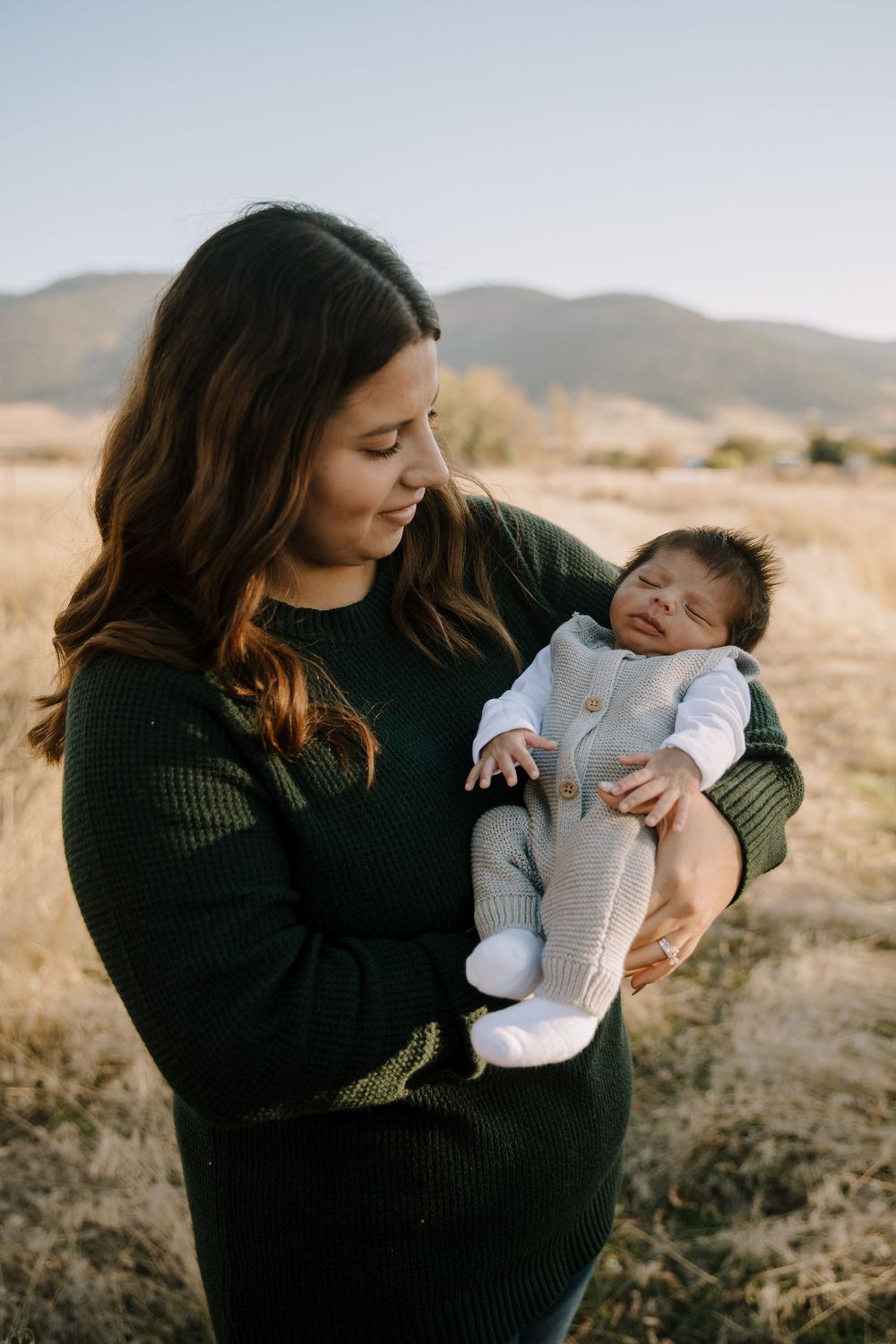 Tender moments between parent and newborn baby against mountain landscape at sunset.