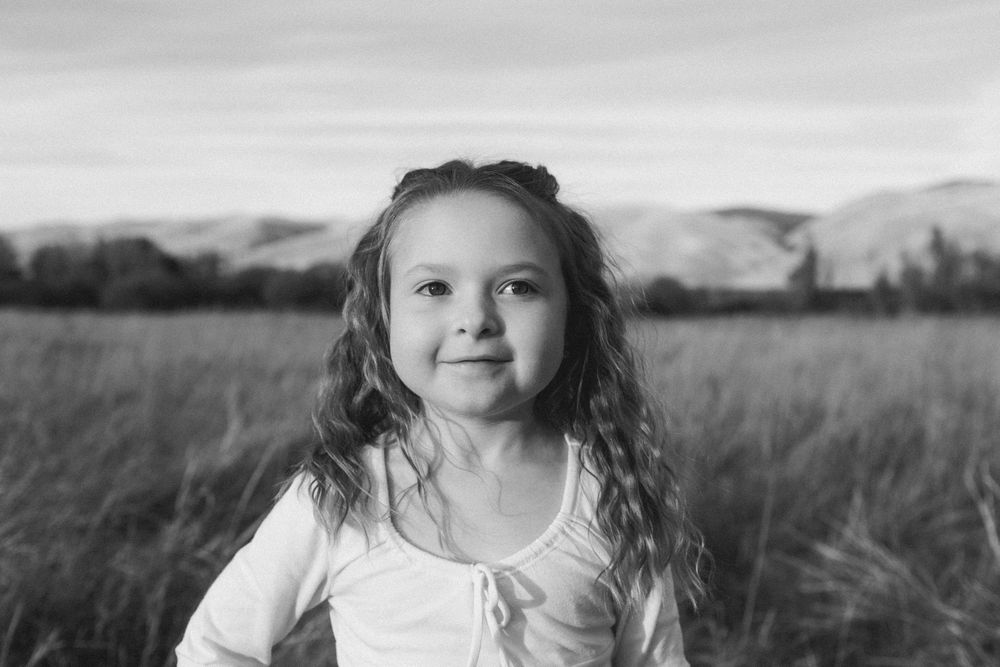 A dreamy portrait in a field of tall grass with mountains visible in the distance.