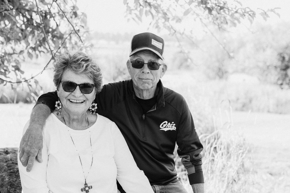 A mature couple in sunglasses poses together outdoors on a bright sunny day.