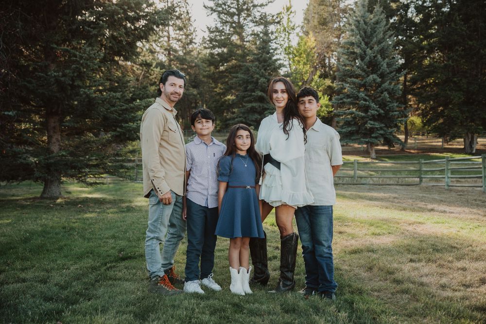 Extended family gathering for outdoor portraits in a park setting with evergreen trees.