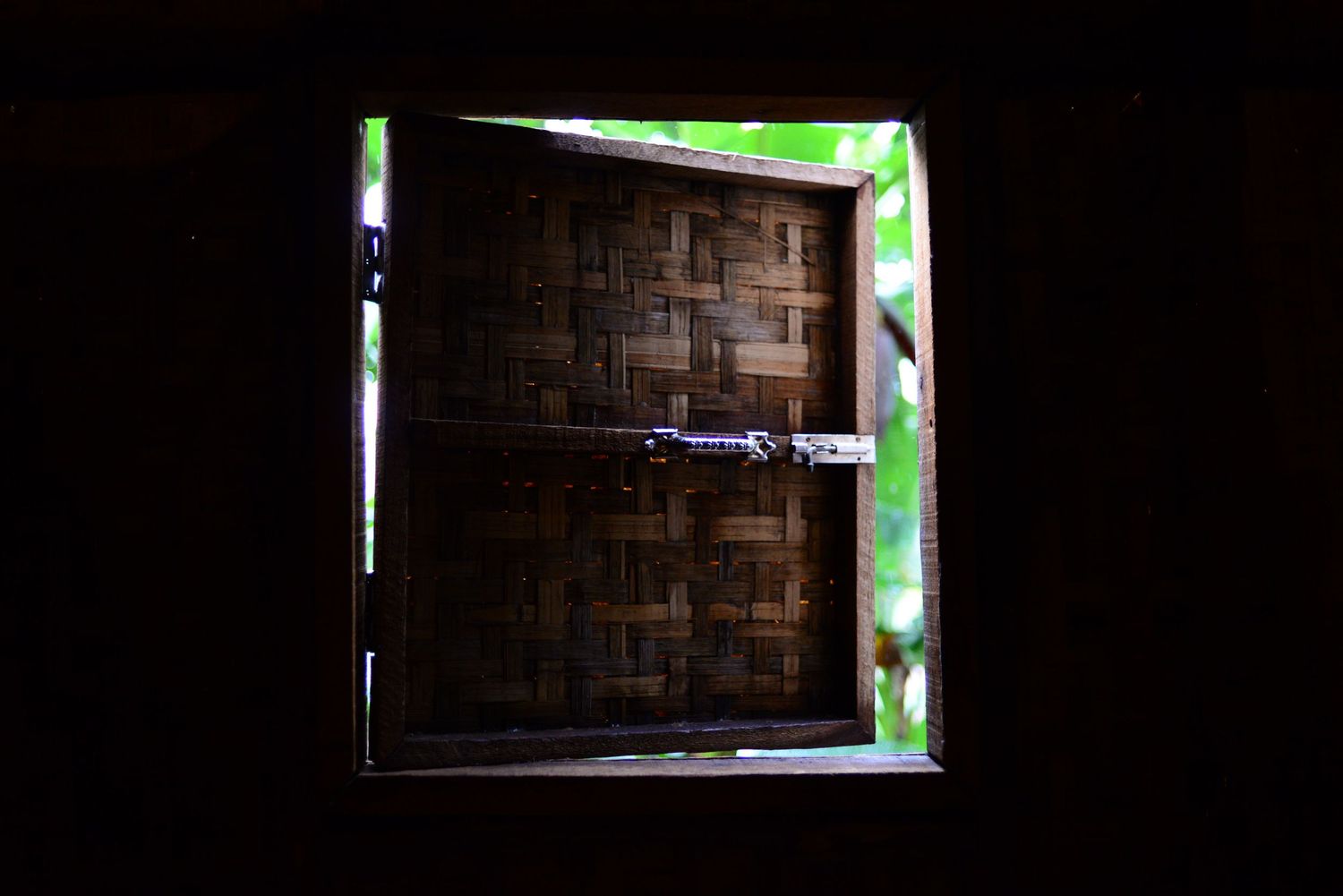 A rustic wooden door illuminated by green light through a window frame in a dark interior.