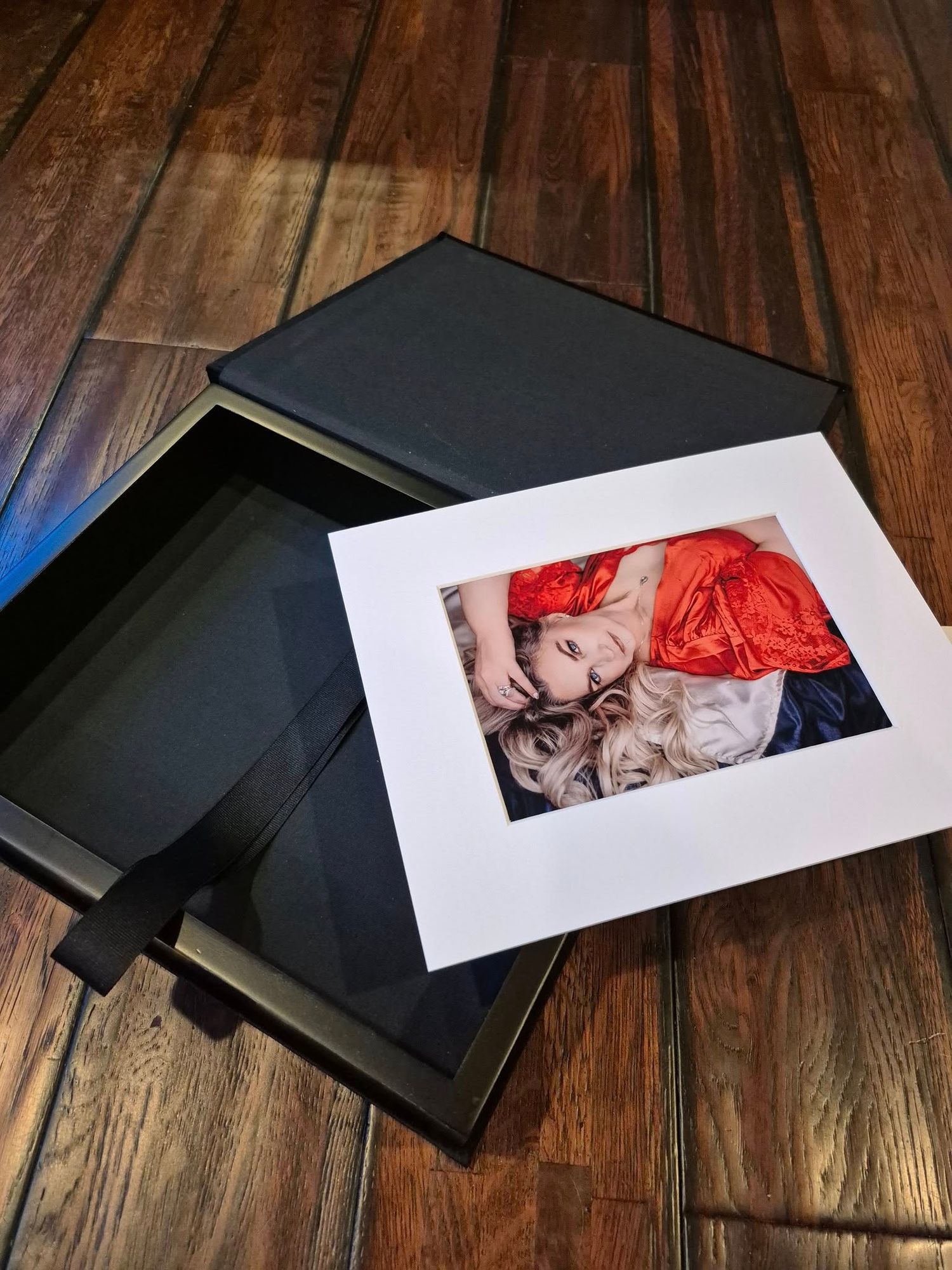Black portfolio boxes with photographic prints displayed on a wooden floor surface.