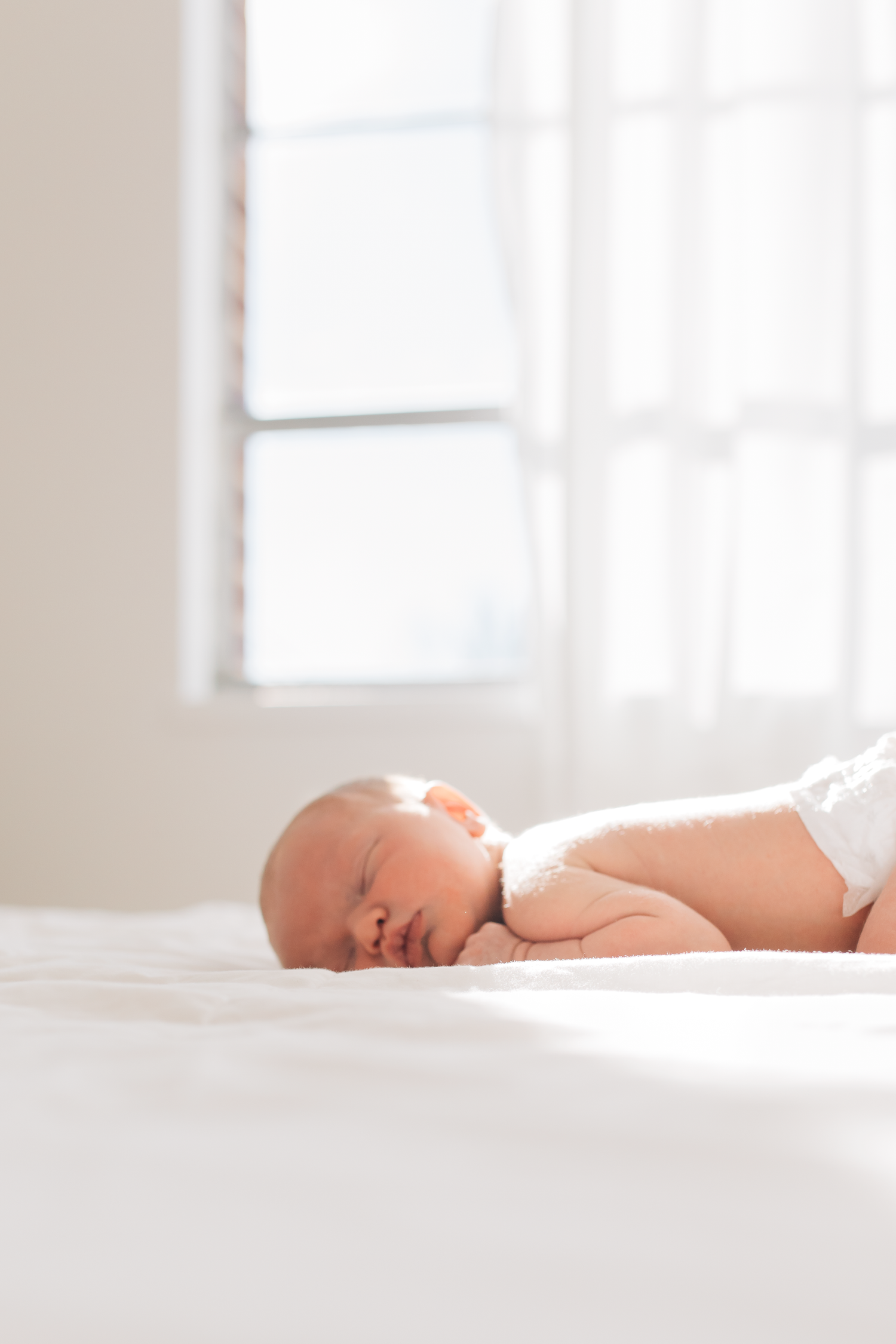 A baby wearing a knit hat lies down while making an adorable expression with wide eyes and open mouth.