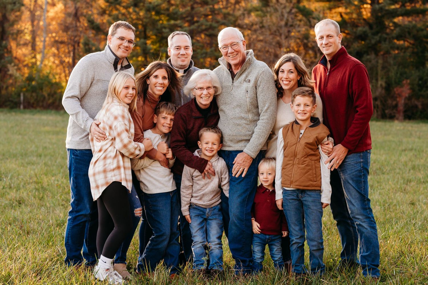 Multi-generational family portrait outdoors with fall foliage in the background.
