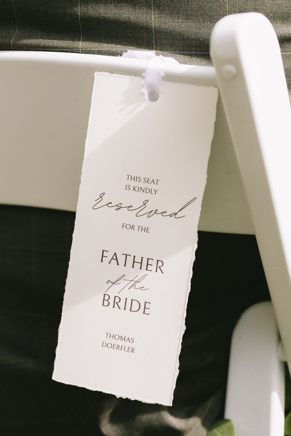 Wedding ceremony seat reservation tag for Father of the Bride hanging on white folding chair.