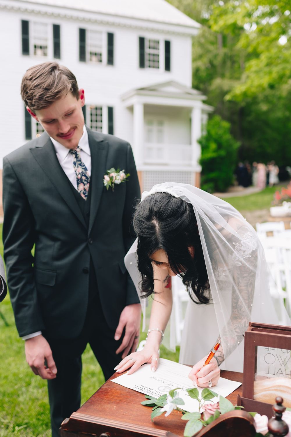 Wedding party members signing documents at a traditional white colonial style building.
