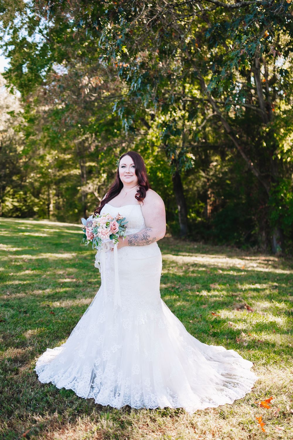 Bride in lace mermaid wedding gown poses in outdoor garden setting.