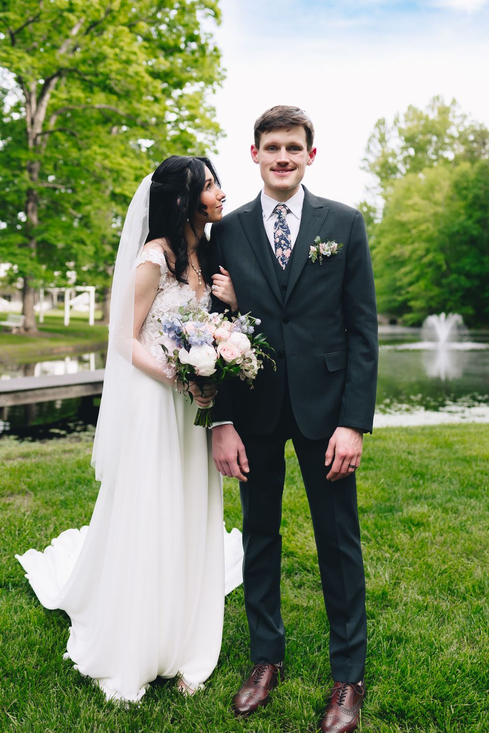 Wedding portraits taken on grassy lawn with fountain and trees in background.