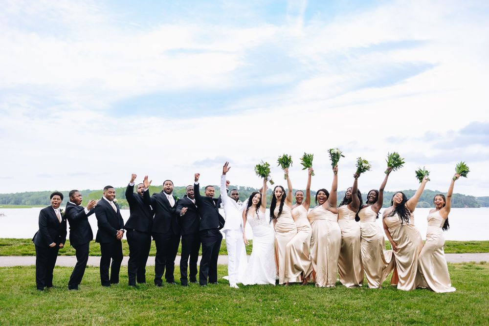 Creative wedding party photo poses on waterfront lawn with dramatic sky background.