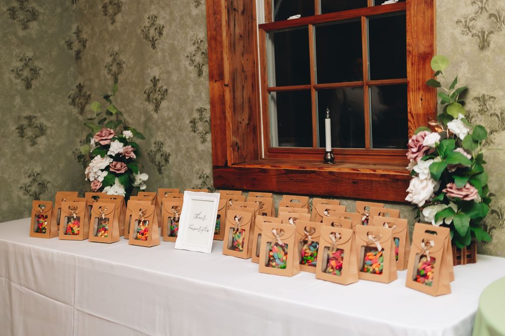 Wedding favor bags lined up on rustic wooden table with decorative window background.