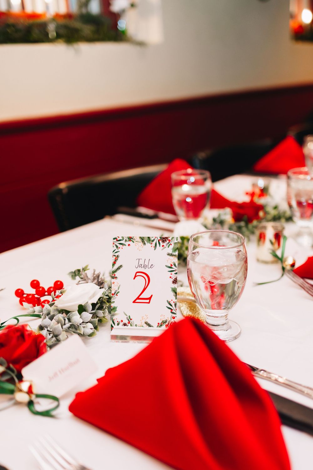 Elegant wedding table setting with red napkins, floral centerpiece and table number card.