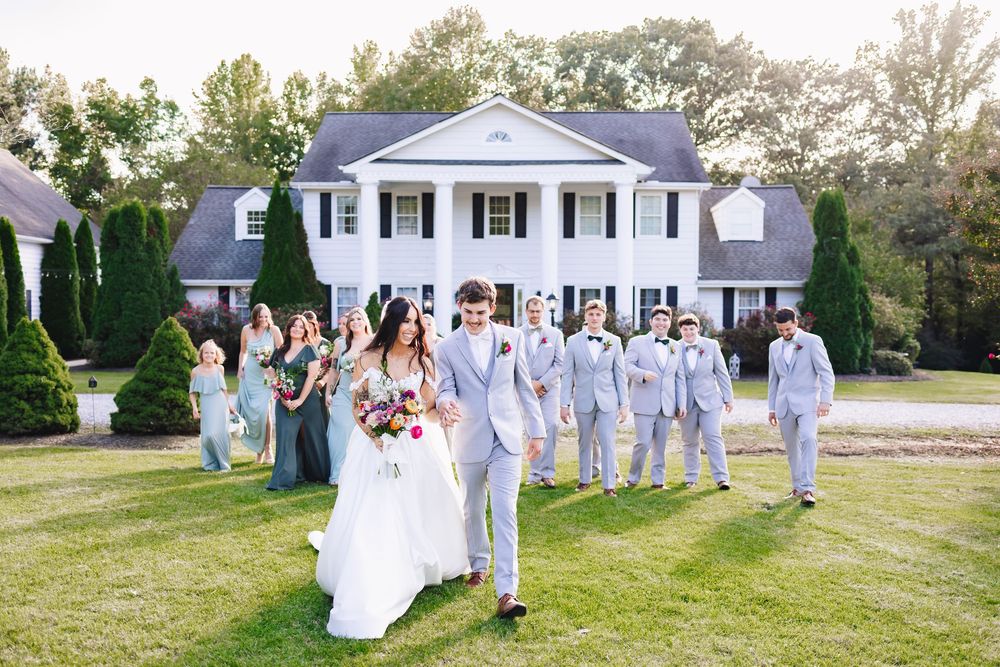 Wedding party gathered in front of elegant white colonial style mansion.