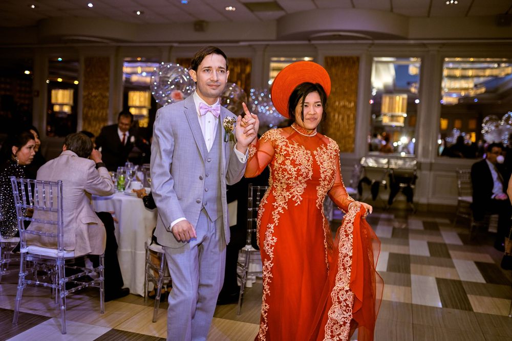 A couple celebrates at their reception with one wearing an ornate orange traditional dress.