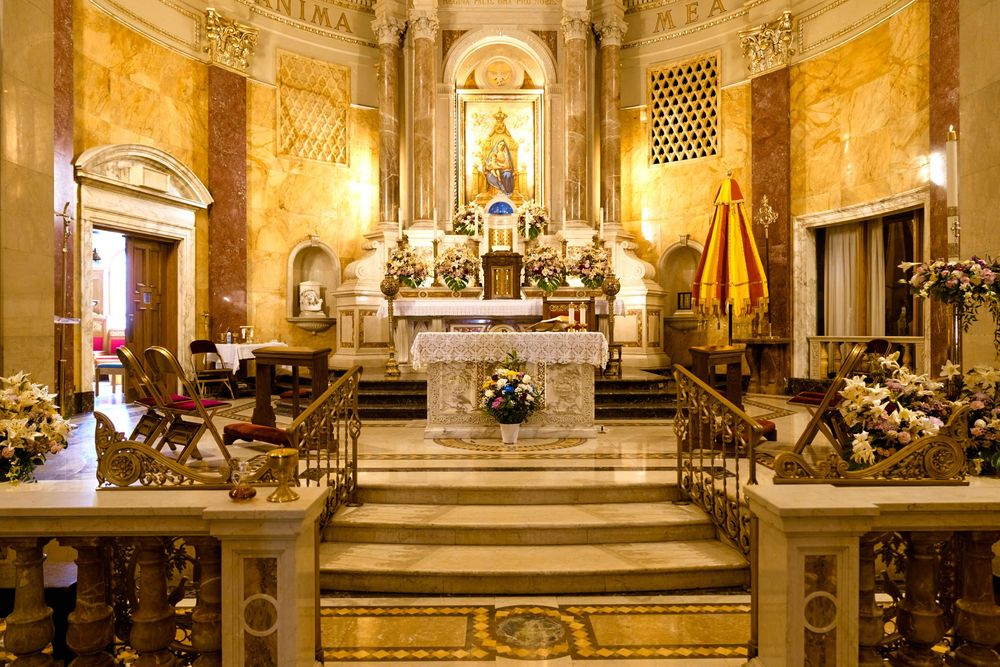 Ornate church altar with marble steps, golden details and decorative floral arrangements.