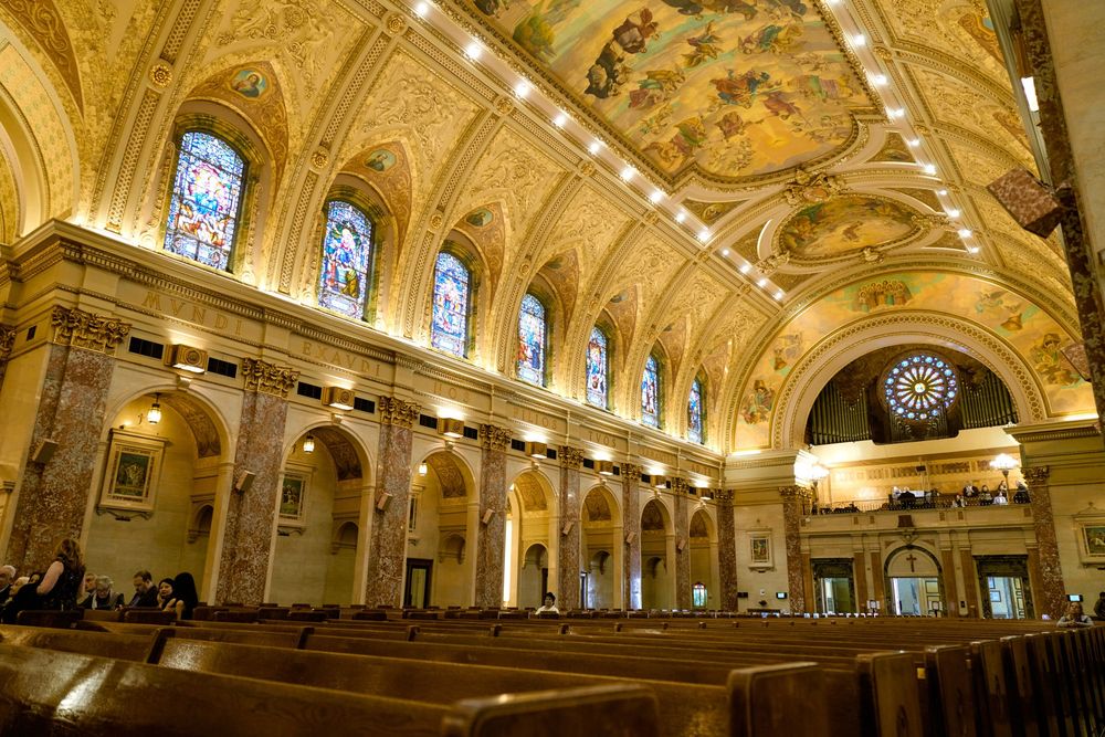 Interior view of an ornate church sanctuary with vaulted ceiling, stained glass windows and rows of wooden pews.