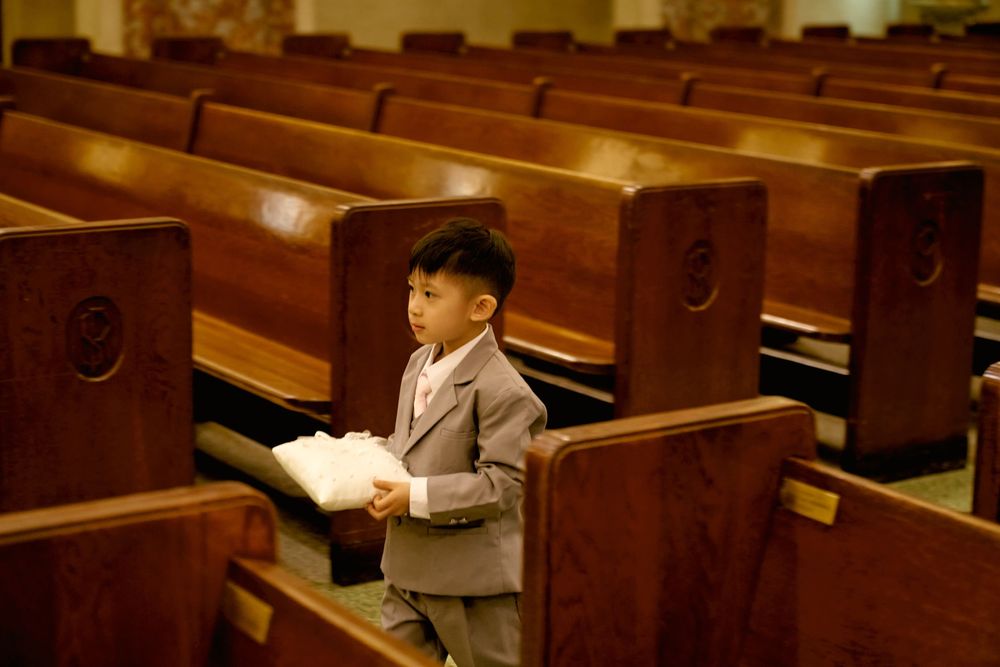 Young attendee in formal attire sitting among wooden church pews.