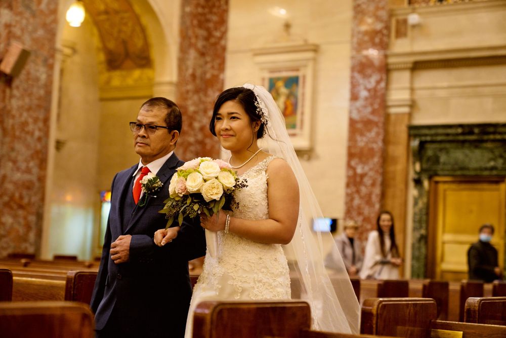 A traditional church wedding ceremony with a couple standing in front of wooden pews holding a white bouquet.