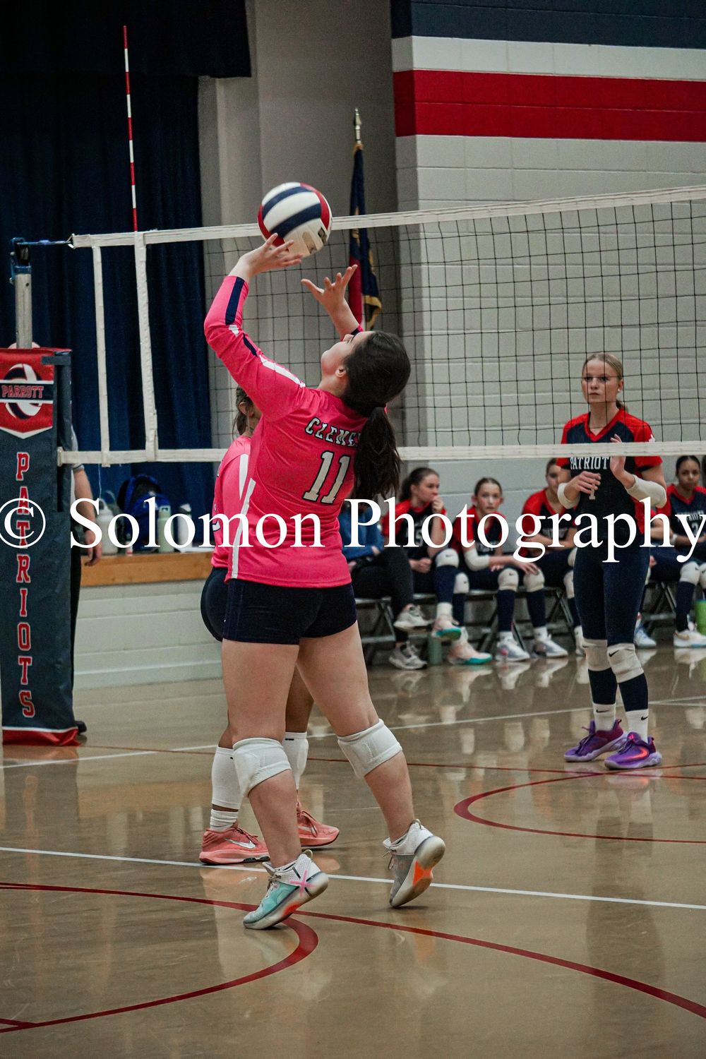 Volleyball player in pink jersey number 11 sets the ball during an indoor high school match.