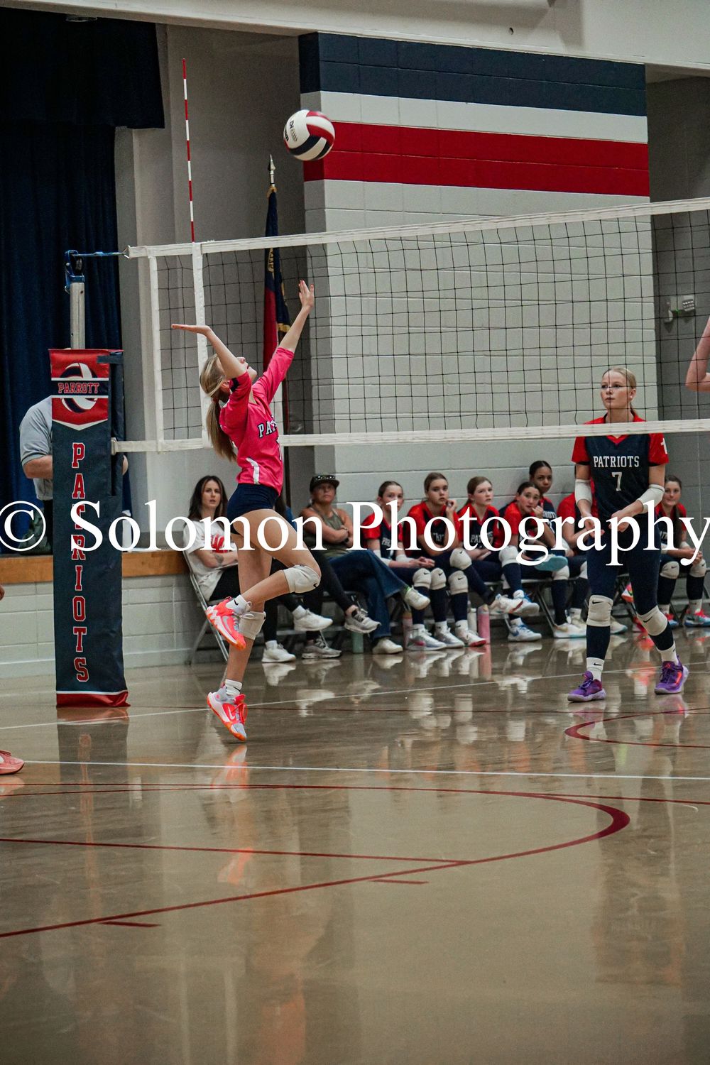 Volleyball player in pink jersey spikes the ball over the net during an indoor match.
