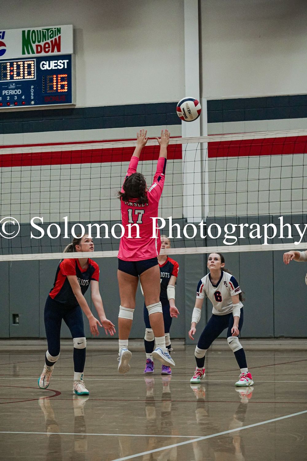 Volleyball player number 17 in pink uniform jumps to block the ball at the net.