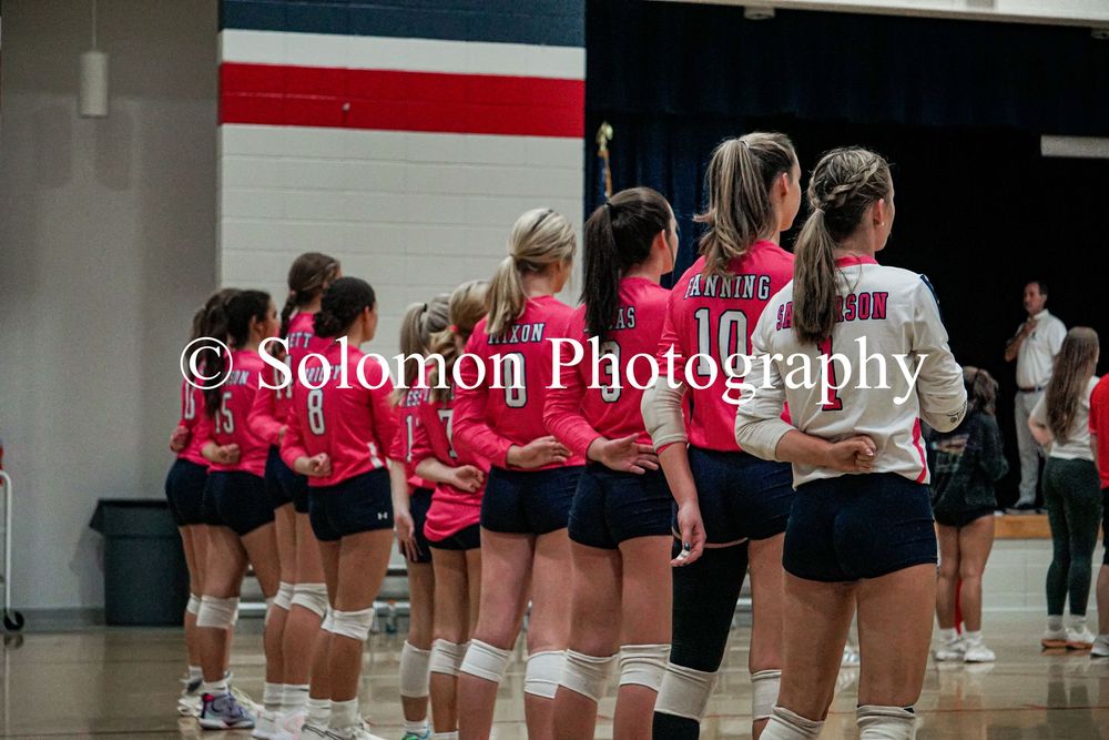Girls volleyball team in pink and navy uniforms lines up on the court before a match.