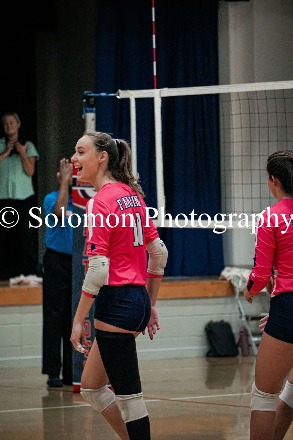 Smiling volleyball player in pink Faith jersey celebrates during an indoor court match.