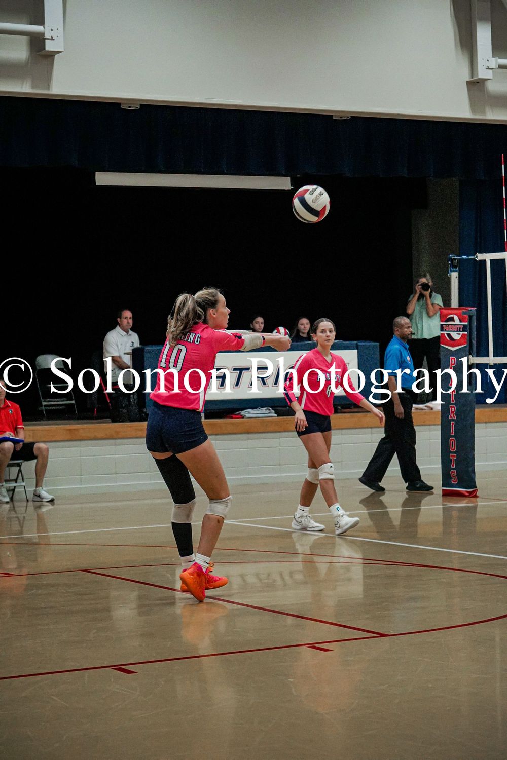 Female volleyball player in pink jersey bumps the ball during an indoor volleyball match.