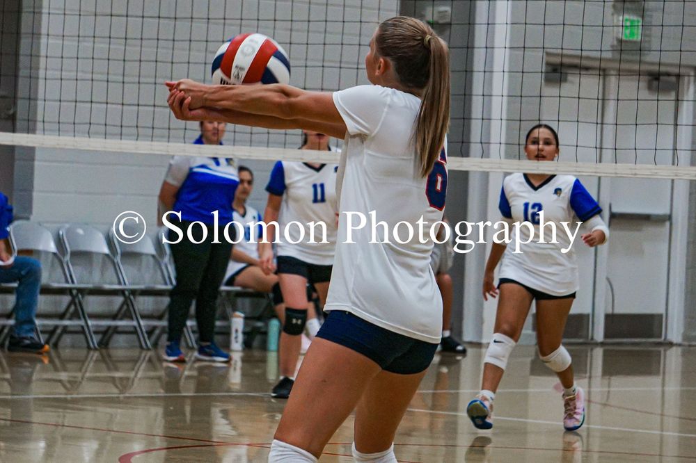 Female volleyball player in white uniform performs forearm pass during indoor volleyball game.