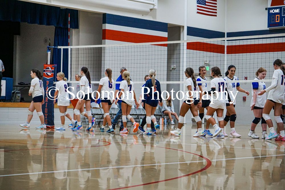 Two high school volleyball teams shake hands at net after indoor match conclusion.