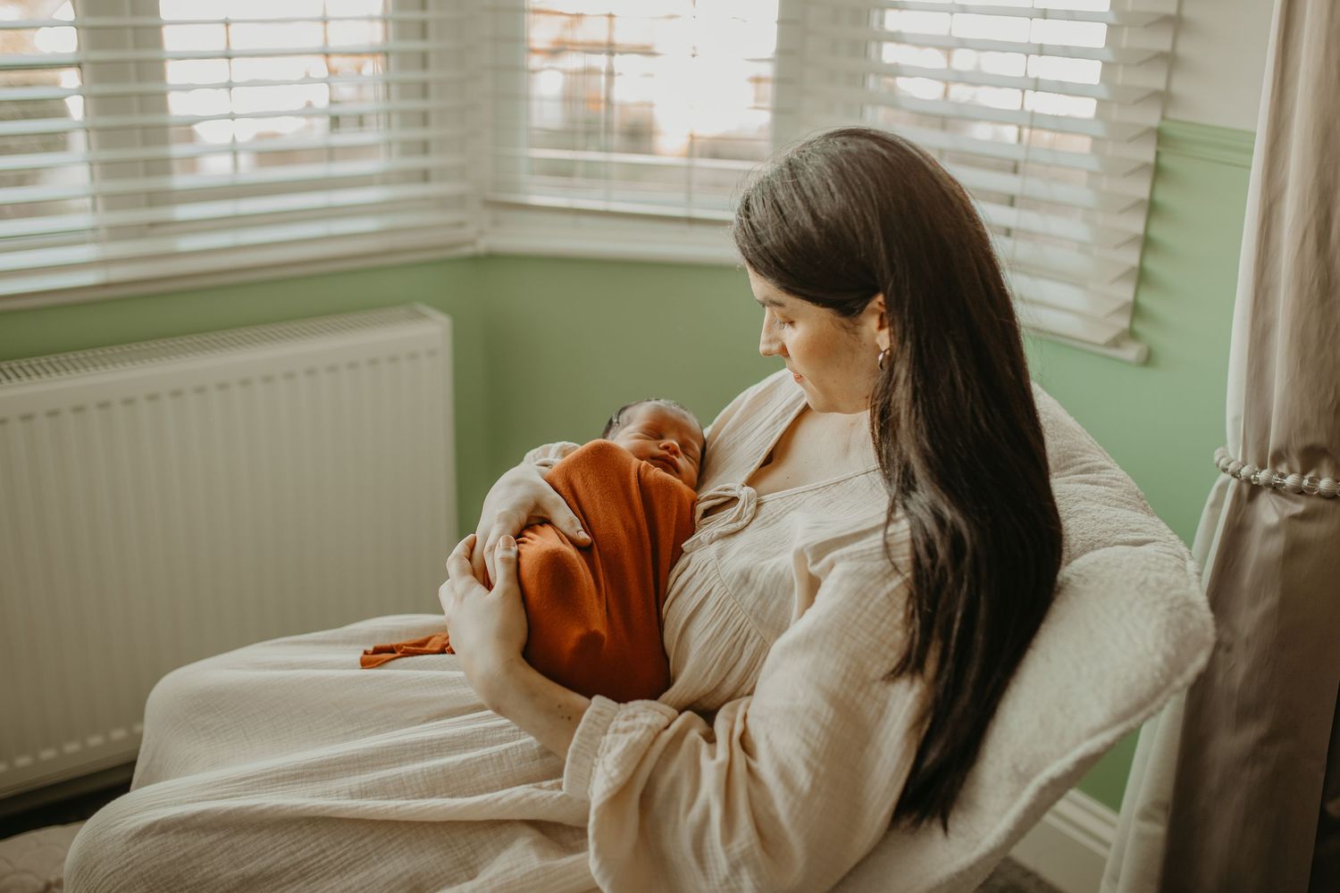 Person lying in soft white bedding near window with natural light streaming in while holding their newborn baby