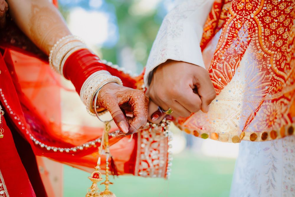 Close-up of Indian bride and groom holding hands in traditional red and gold wedding attire with mehndi.