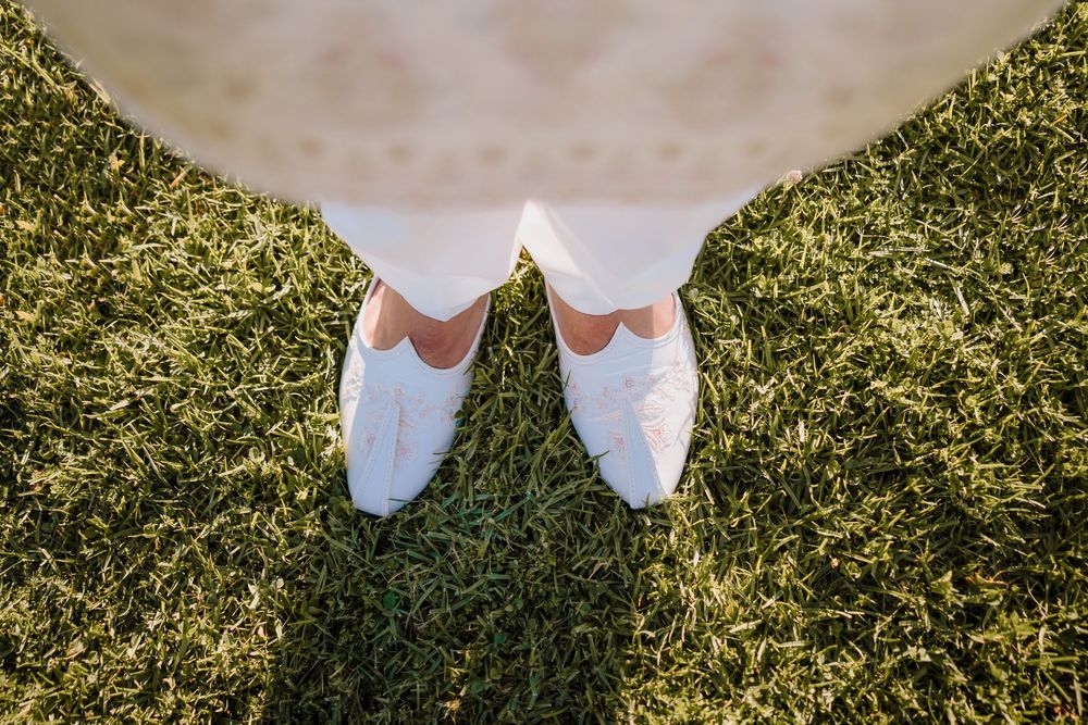 Top-down view of white bridal shoes on lush green grass, perfect for a wedding day outdoor ceremony.