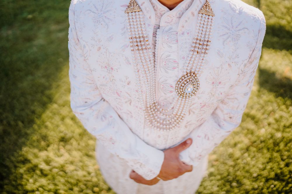 Close-up of Indian groom wearing white embroidered sherwani with layered pearl necklaces.