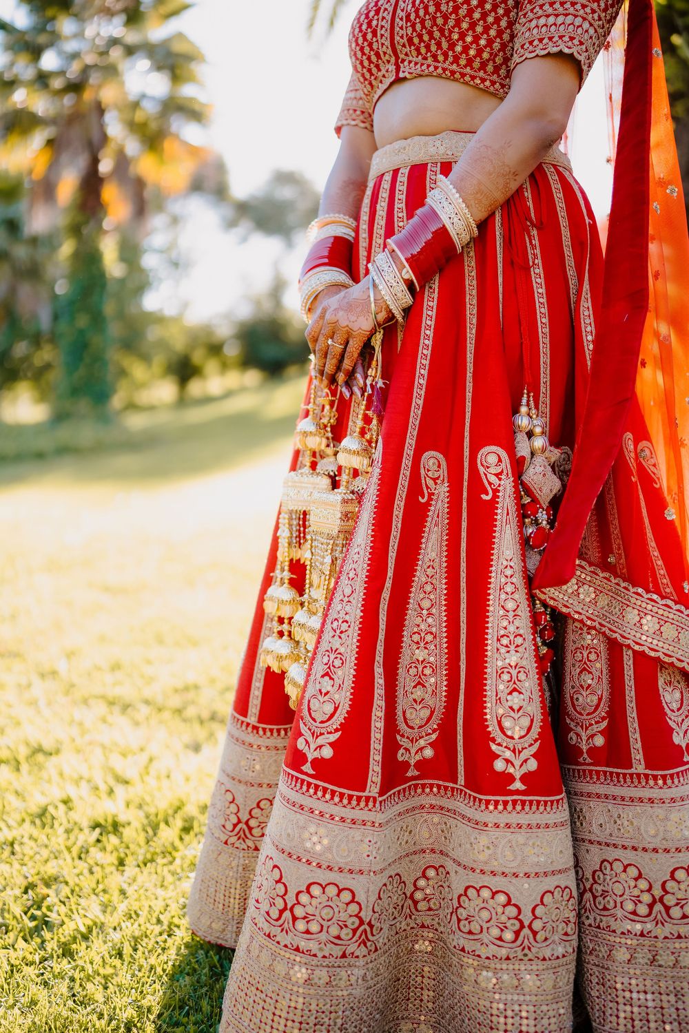 Indian bride in red and gold lehenga with bangles and kalire wedding accessories.