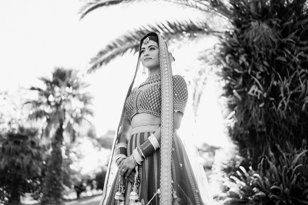 Bride in traditional Indian lehenga posing gracefully under palm trees in black and white photo.