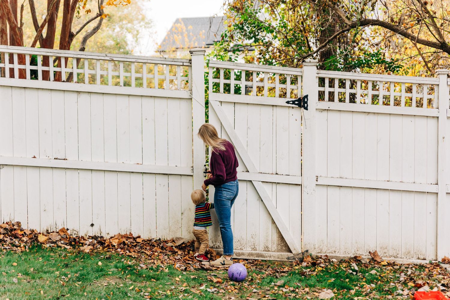 Mother and young son standing in front of a white picket fence in autumn in a backyard.