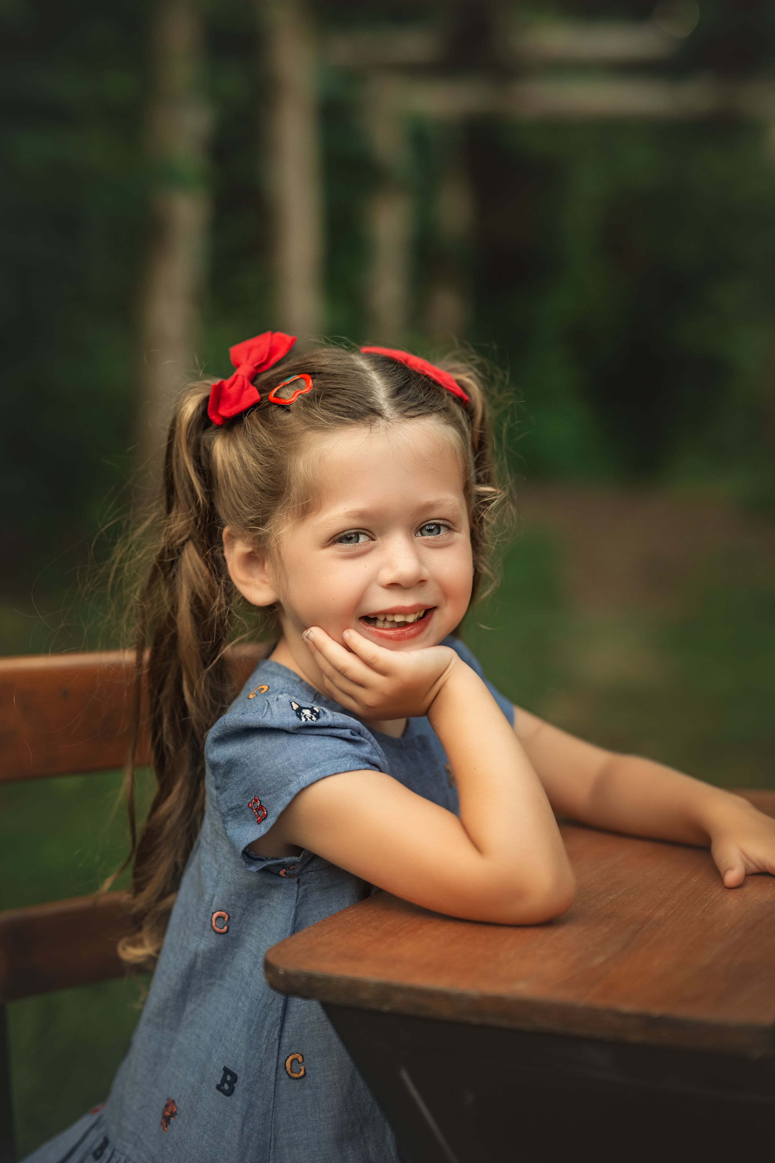 A sequence of candid moments showing a young girl in denim sitting at a wooden school desk in a forest setting.