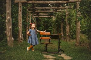 Rustic school desk scene under wooden pergola with joyful student in denim dress.