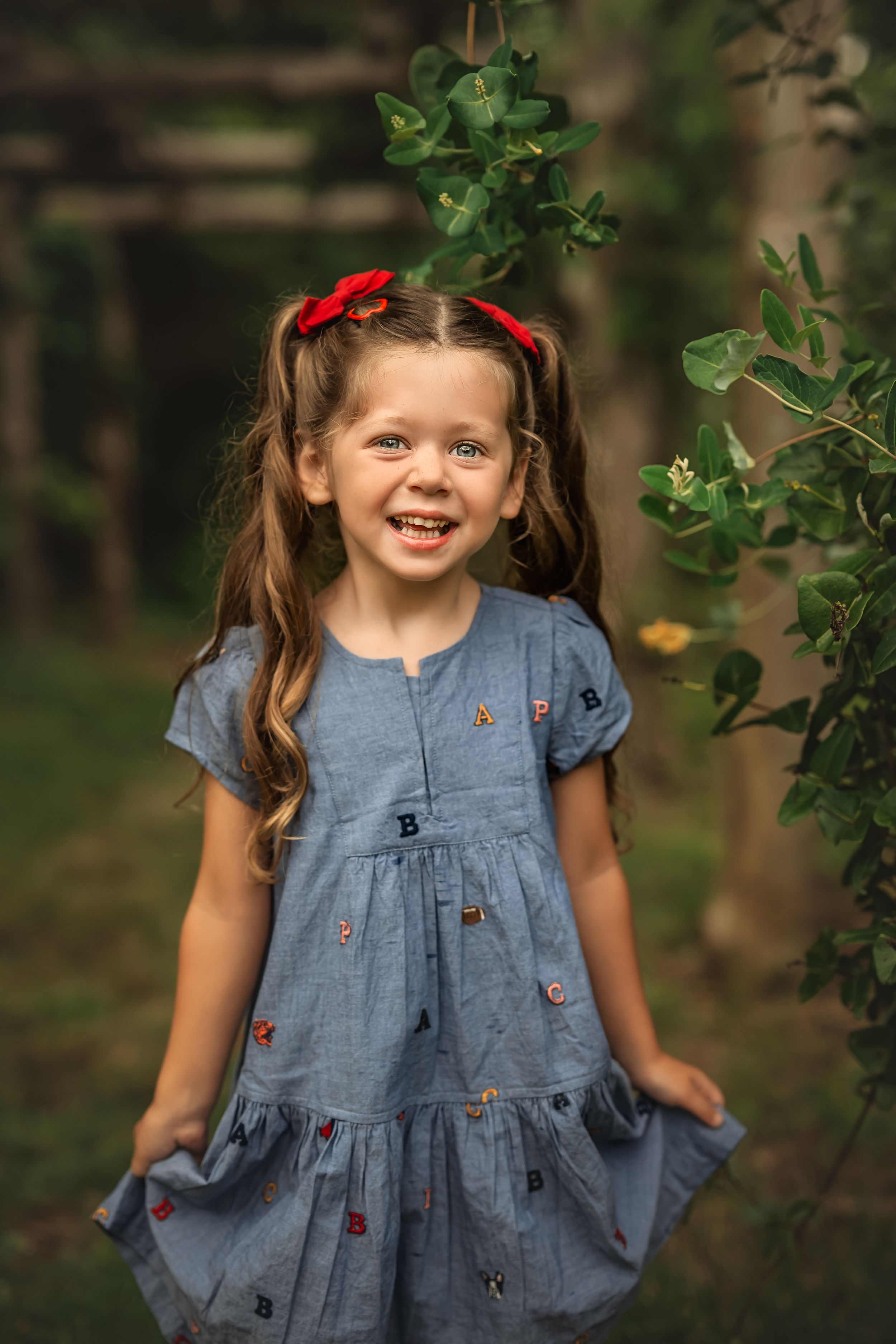 Young student wearing blue embroidered dress smiles brightly in garden setting.