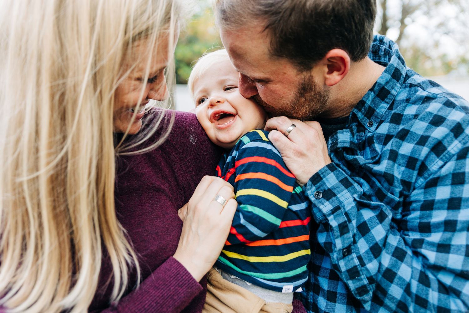 A family shares tender moments and laughter while posing together in outdoor fall portraits wearing coordinated outfits.