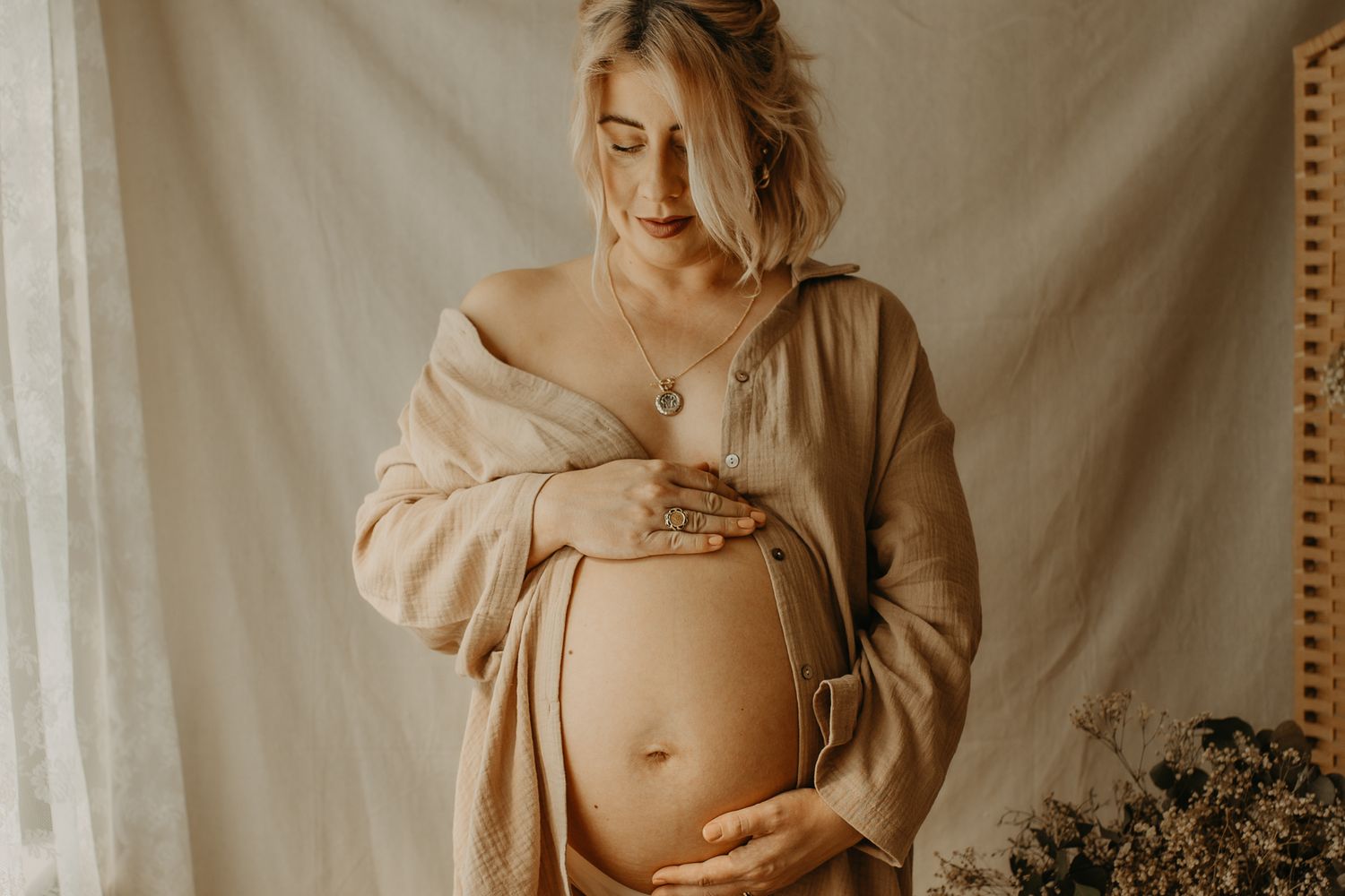 Maternity photo with soft beige tones capturing a pregnant person in a cozy sweater against a neutral backdrop.