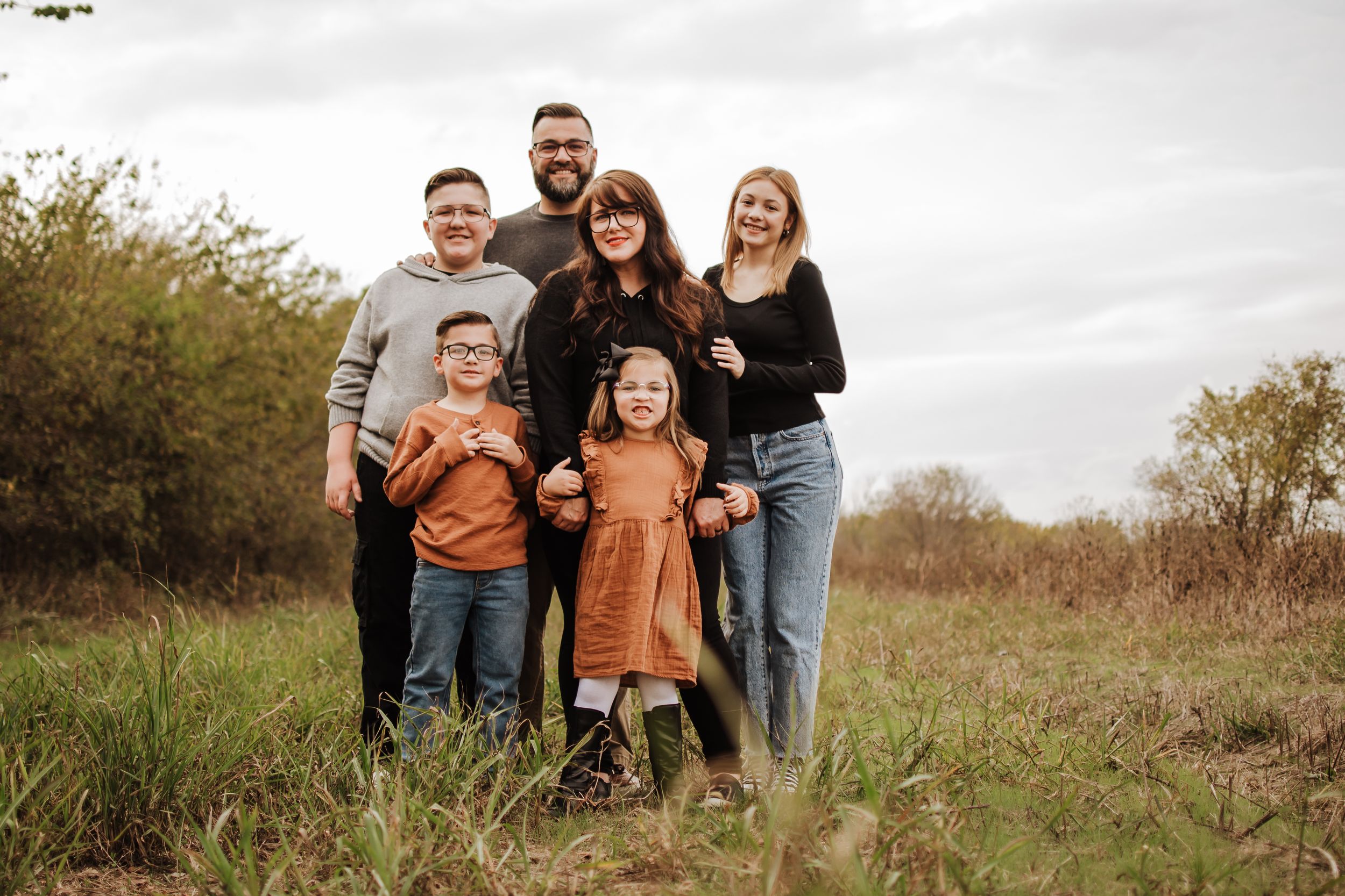 A happy family of five poses together in a rustic field during golden hour.