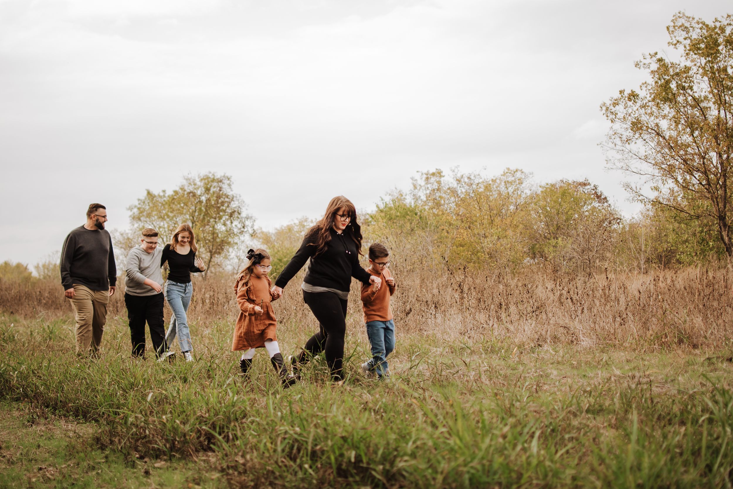 A family enjoying a casual walk together through tall grass in an autumn field.